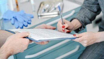Imagem mostra ambiente médico no qual paciente assina documento em prancheta